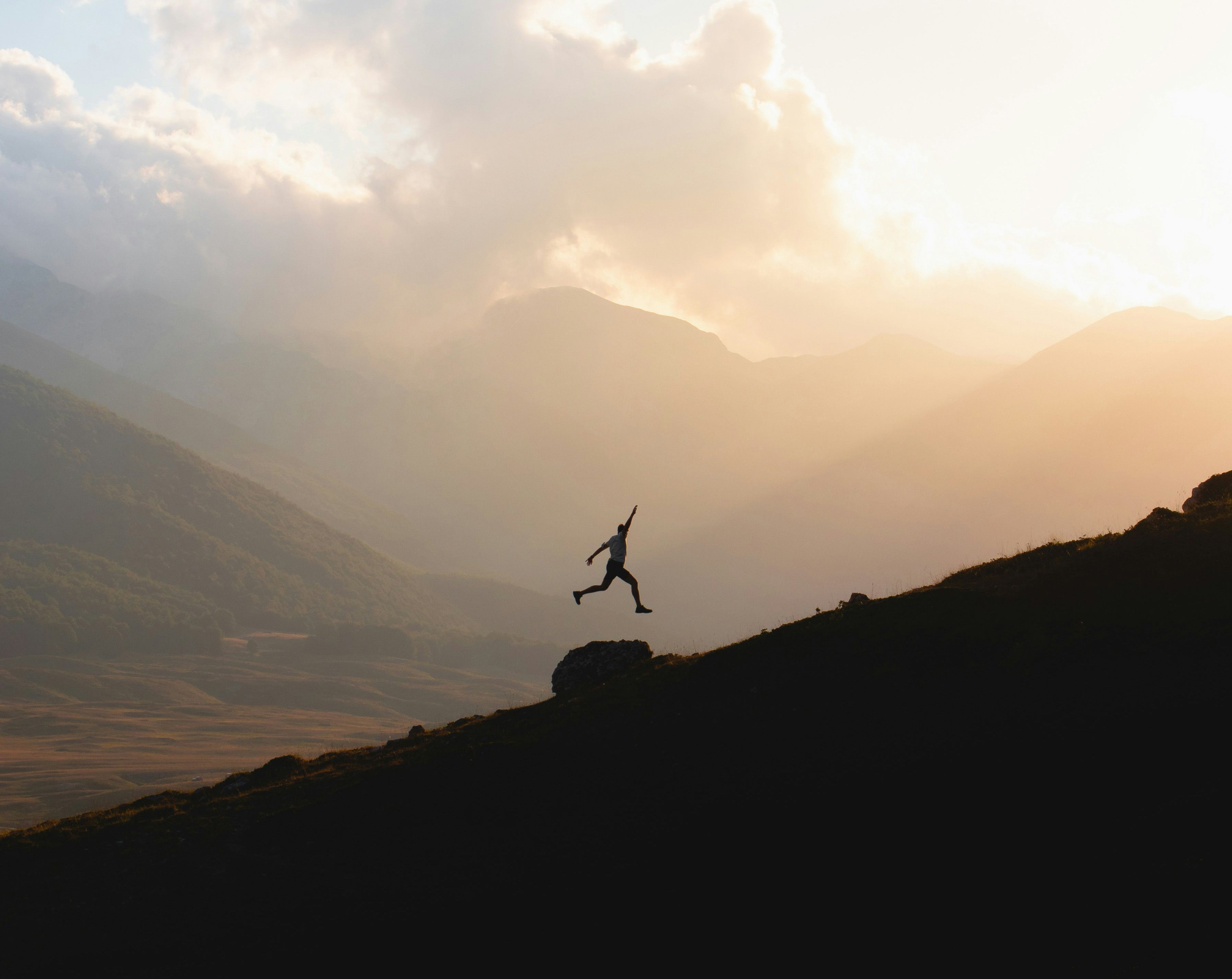 Silhouette of a man jumping over a rock on a hillside